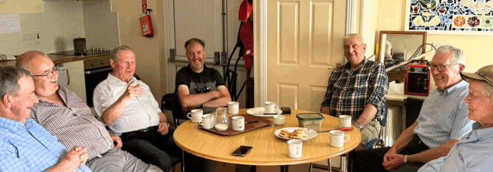 7 Elderly Men sit around a table to enjoy tea and scones