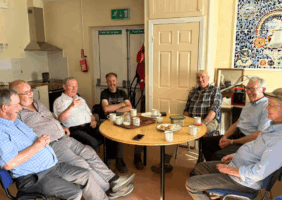 7 Elderly Men sit around a table to enjoy tea and scones