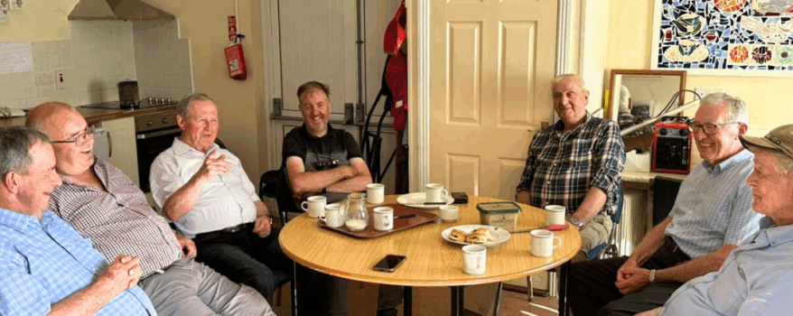 7 Elderly Men sit around a table to enjoy tea and scones