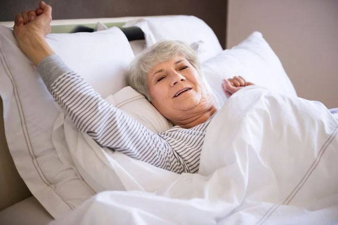 Elderly woman stretching in her bed