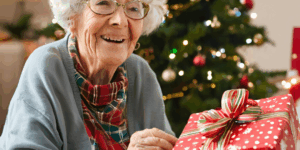 Elderly woman sitting by the Christmas tree with a wrapped present