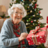 Elderly woman sitting by the Christmas tree with a wrapped present