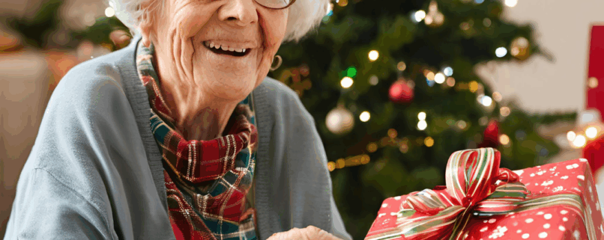 Elderly woman sitting by the Christmas tree with a wrapped present